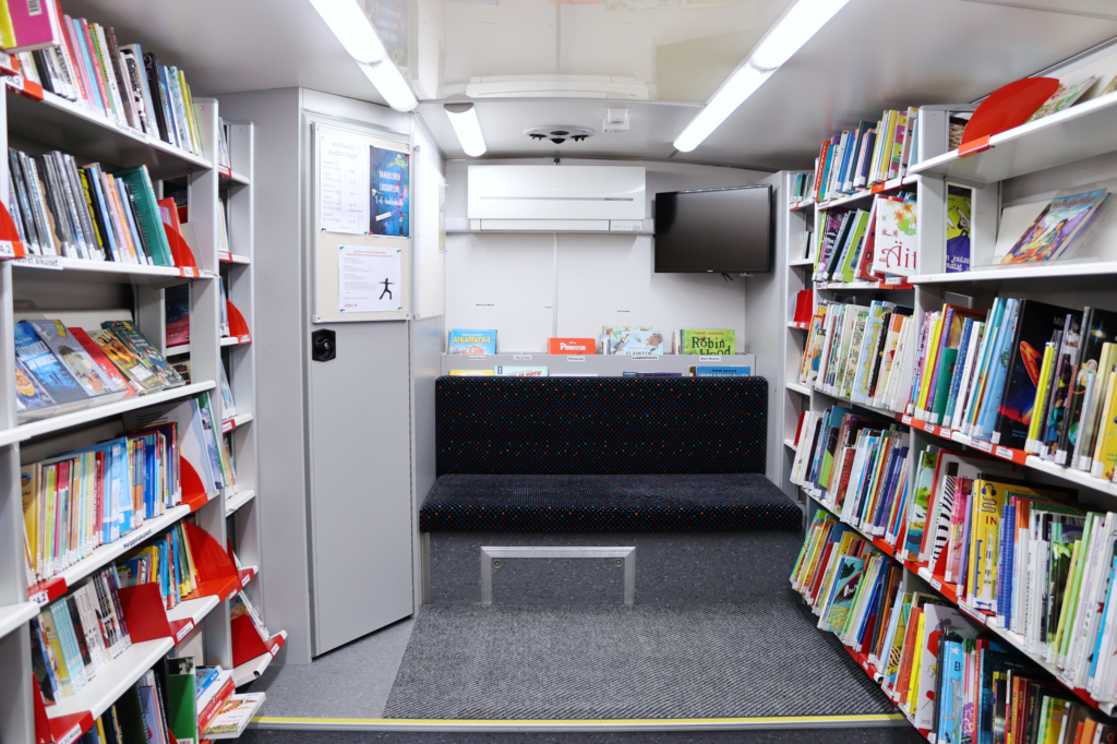 Kuvassa on kirjastoauton peräosan lasten ja nuorten osasto. Kirjahyllyjä ja istuin.
