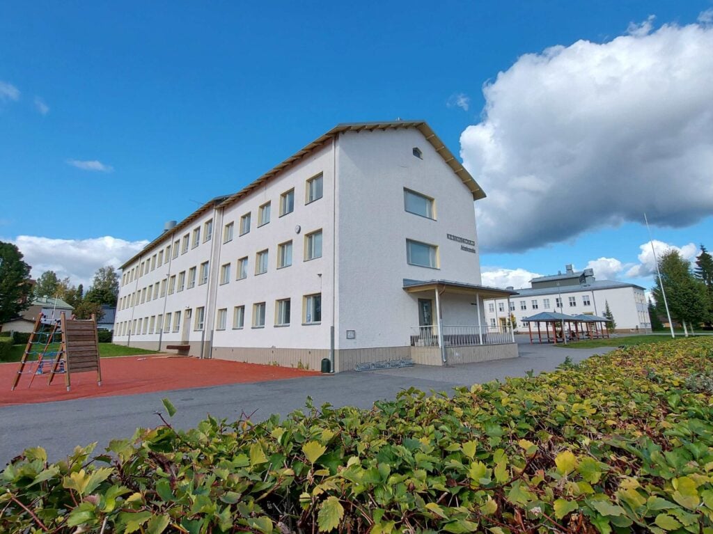 Koulun piha-alue. Kaksi kivirakennusta, pyöräkatokset ja leikkialue.