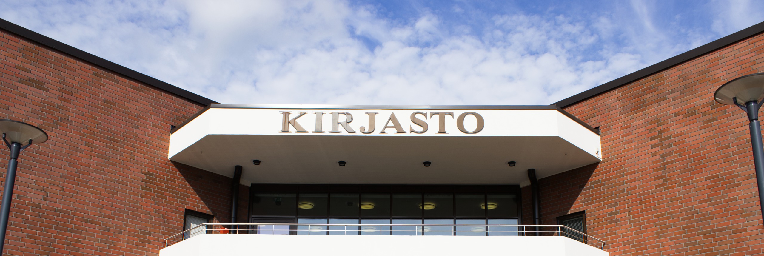 Kuvassa on Lieksan kirjaston julkisivun Kirjasto-kyltti. Taustalla näkyy taivasta.