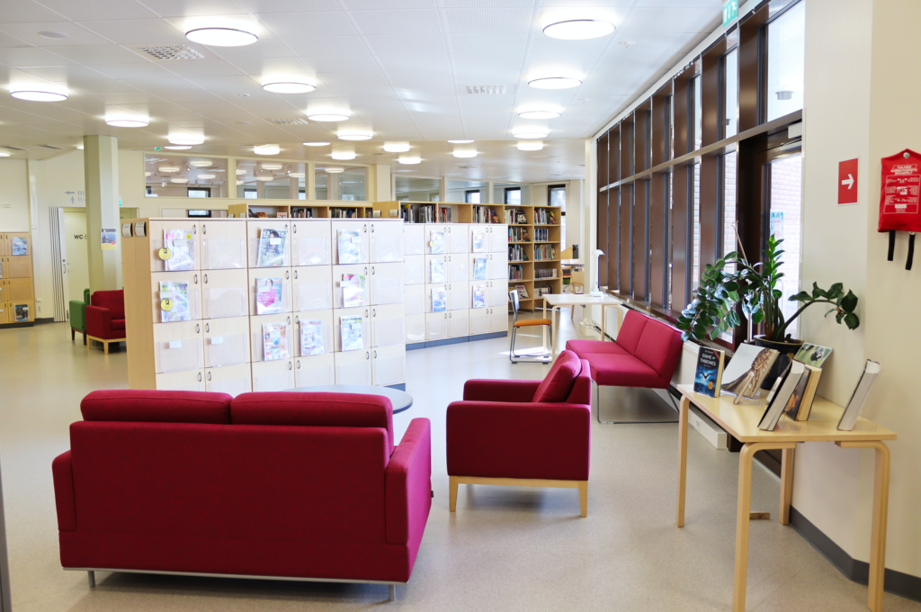 Kuvassa on Lieksan kirjaston lehtiosastoa. Kuvan etualalla on sohvaryhmä. Kauempana on lehtikaappeja ja kirjahyllyjä.