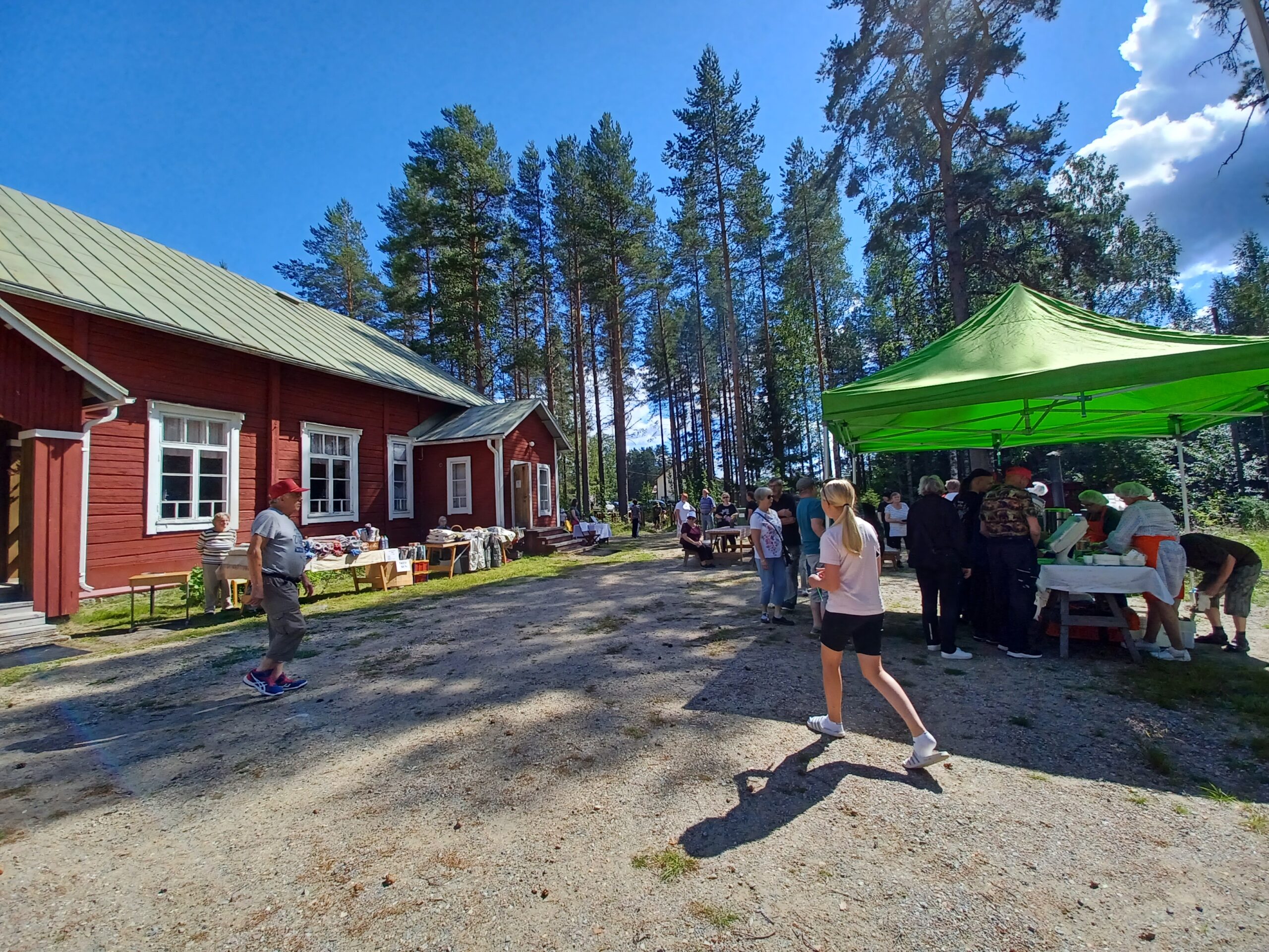 Punainen hirsitalo, jonka edessä paljon ihmisiä ja telttakatos, jonne osa ihmisistä jonottaa.