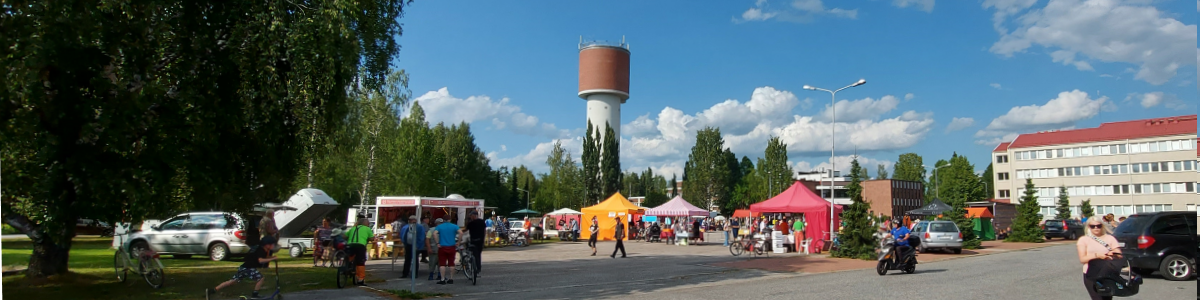 Tori alue telttoineen. Ihmisiä torilla, on kesä. Taustalla näkyy korkea vesitorni.